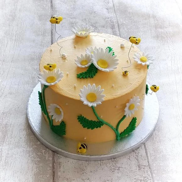 Tarta amarilla con margaritas y pequeñas abejas